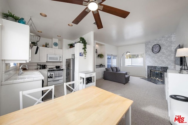 kitchen featuring white appliances, white cabinets, sink, ceiling fan, and tile counters