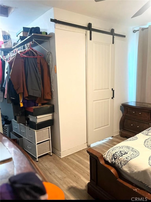 bedroom featuring ceiling fan, a barn door, and light wood-type flooring