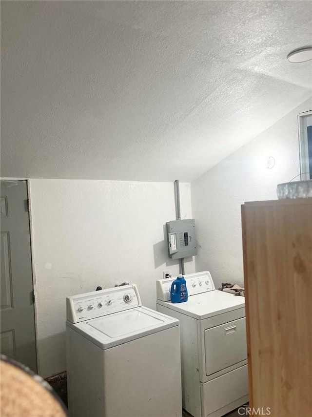 clothes washing area featuring a textured ceiling, washer and clothes dryer, and electric panel