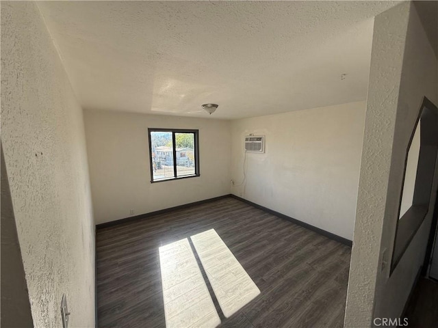 unfurnished room featuring a wall mounted air conditioner, a textured ceiling, and dark wood-type flooring