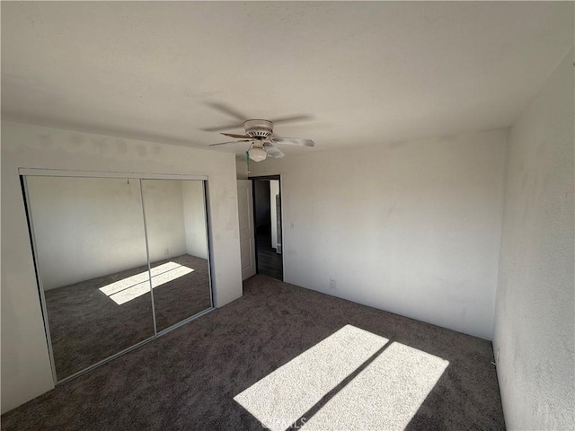 unfurnished bedroom featuring dark colored carpet, a closet, and ceiling fan