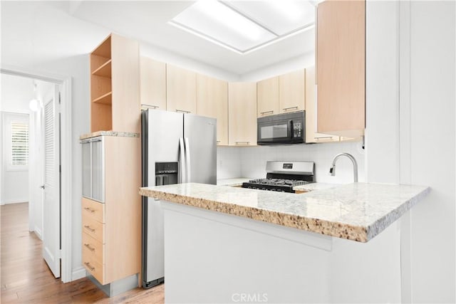 kitchen with light brown cabinetry, light hardwood / wood-style floors, kitchen peninsula, stainless steel appliances, and light stone countertops