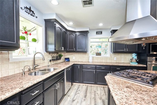 kitchen with sink, backsplash, light hardwood / wood-style floors, island range hood, and appliances with stainless steel finishes