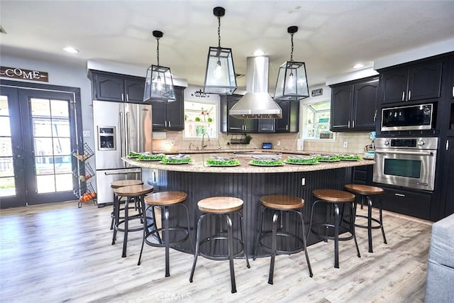 kitchen featuring a center island, light hardwood / wood-style flooring, wall chimney range hood, and appliances with stainless steel finishes