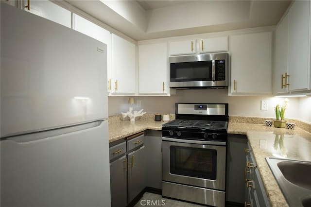 kitchen featuring gray cabinetry, white cabinetry, sink, light stone countertops, and appliances with stainless steel finishes