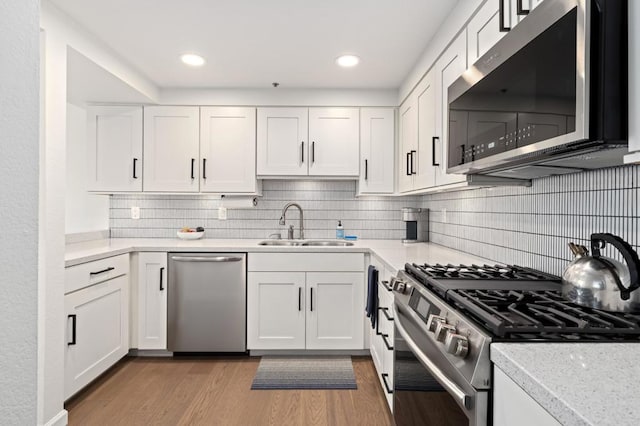 kitchen with appliances with stainless steel finishes, light wood-type flooring, white cabinetry, and sink