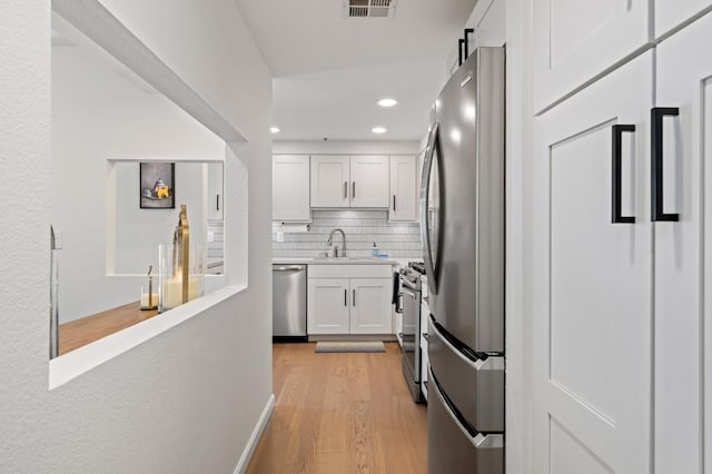 kitchen featuring appliances with stainless steel finishes, light wood-type flooring, white cabinetry, and sink