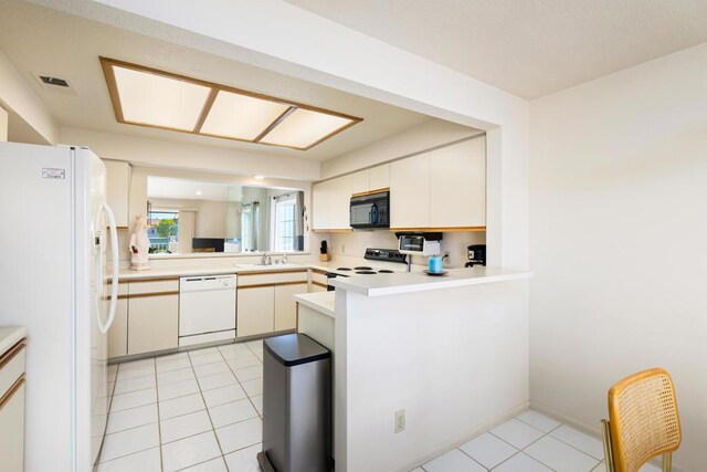 kitchen featuring kitchen peninsula, white appliances, sink, light tile patterned floors, and white cabinetry