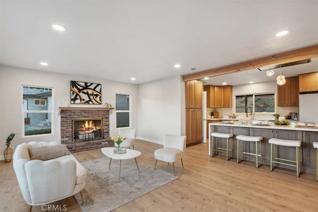 living room with a brick fireplace, light hardwood / wood-style floors, beamed ceiling, and a healthy amount of sunlight