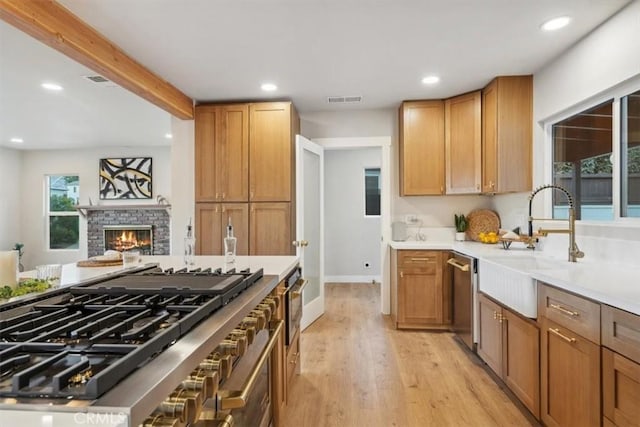 kitchen featuring appliances with stainless steel finishes, sink, light wood-type flooring, a brick fireplace, and beam ceiling