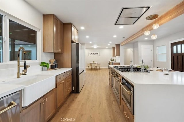 kitchen with appliances with stainless steel finishes, a kitchen island, light hardwood / wood-style floors, sink, and hanging light fixtures