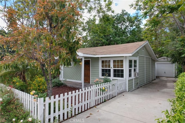 bungalow-style home featuring driveway, an outdoor structure, a fenced front yard, roof with shingles, and a garage
