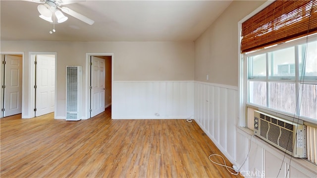 unfurnished room featuring a heating unit, ceiling fan, light wood-type flooring, cooling unit, and wainscoting