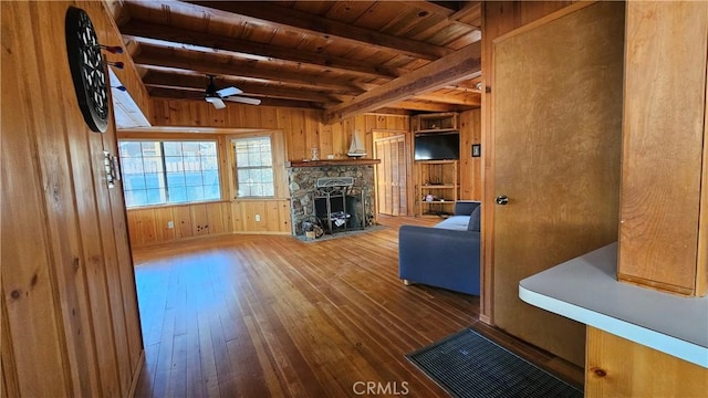 unfurnished living room featuring ceiling fan, beamed ceiling, hardwood / wood-style floors, wooden walls, and a fireplace