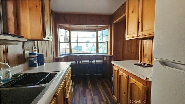 kitchen with dark hardwood / wood-style flooring, white refrigerator, wooden walls, and sink