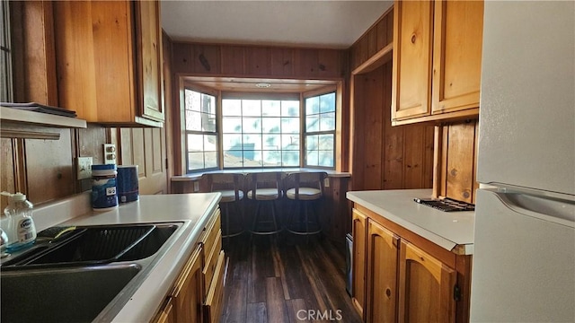 kitchen with wooden walls, sink, white fridge, and dark wood-type flooring