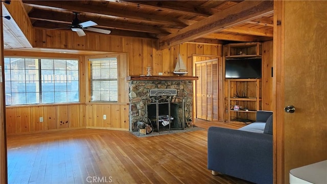 living room with a fireplace, hardwood / wood-style floors, ceiling fan, and wood walls