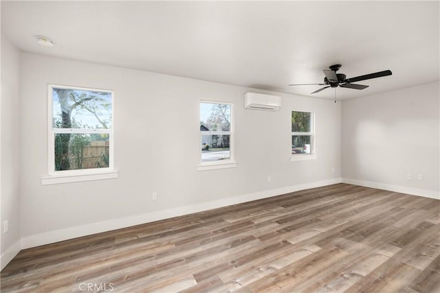 empty room featuring ceiling fan, a healthy amount of sunlight, light hardwood / wood-style floors, and a wall unit AC