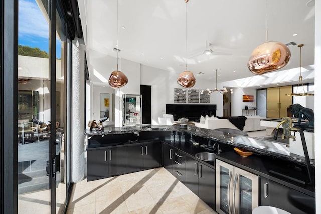 kitchen featuring ceiling fan, beverage cooler, sink, pendant lighting, and dark stone countertops