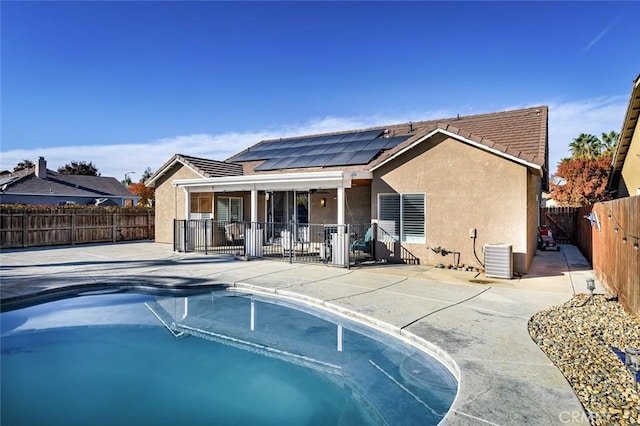 rear view of property featuring solar panels, a patio area, a fenced in pool, and cooling unit