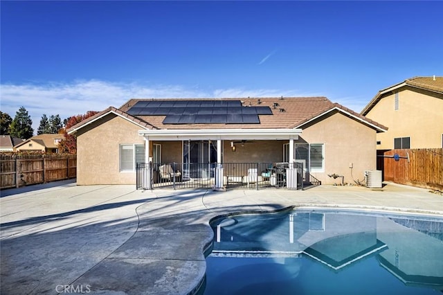 rear view of house with solar panels, a patio, a fenced in pool, and central AC unit