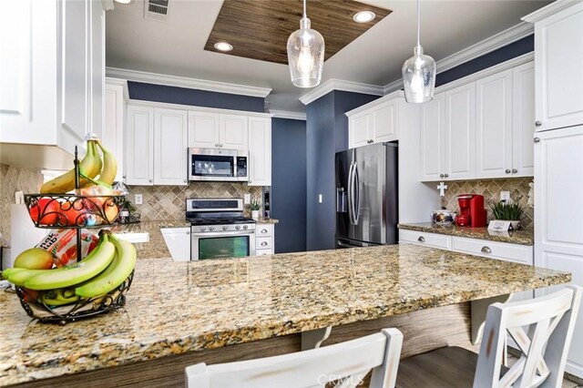 kitchen with white cabinets, ornamental molding, appliances with stainless steel finishes, decorative light fixtures, and a kitchen bar