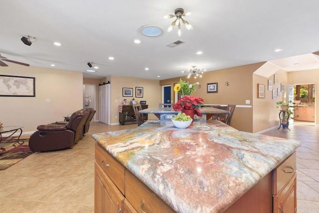 kitchen with light stone countertops, a kitchen island, ceiling fan with notable chandelier, and light tile patterned floors