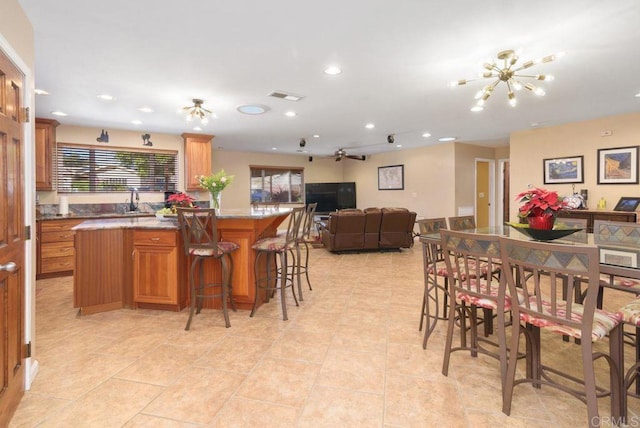 kitchen with a breakfast bar, a center island, a notable chandelier, light tile patterned flooring, and light stone counters