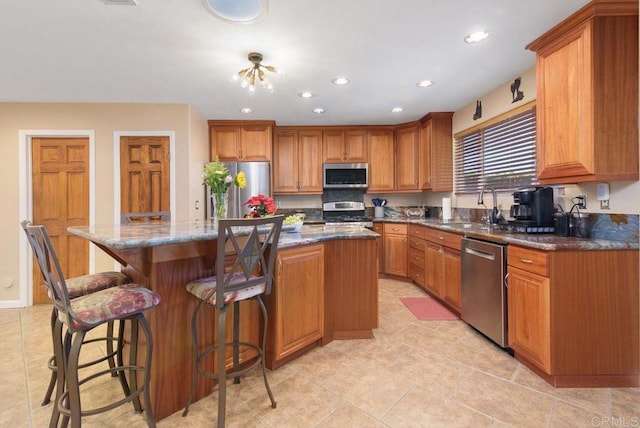 kitchen with sink, a center island, dark stone counters, a breakfast bar area, and appliances with stainless steel finishes