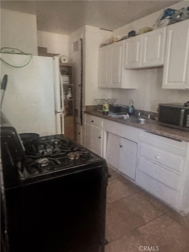 kitchen with tile patterned floors, white refrigerator, white cabinetry, and black electric range