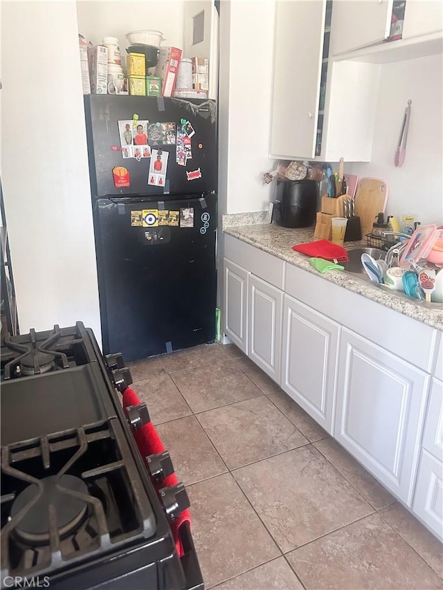 kitchen featuring black refrigerator, range, white cabinets, and light tile patterned floors