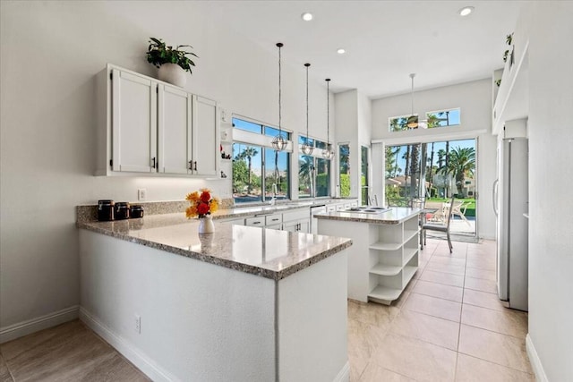 kitchen featuring kitchen peninsula, pendant lighting, white cabinets, and light stone counters