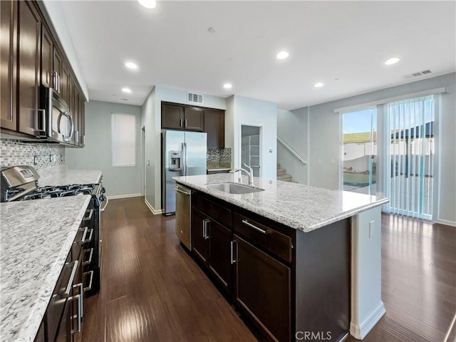 kitchen with sink, dark wood-type flooring, stainless steel appliances, decorative backsplash, and a center island with sink