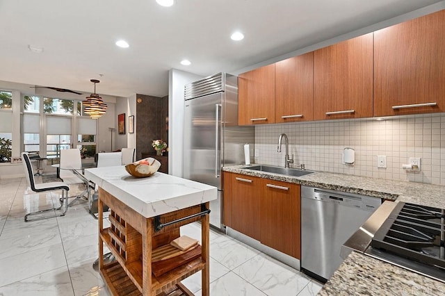 kitchen featuring tasteful backsplash, light stone counters, stainless steel appliances, sink, and hanging light fixtures