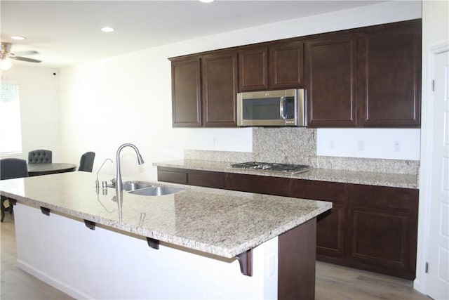 kitchen with appliances with stainless steel finishes, a kitchen island with sink, sink, light hardwood / wood-style floors, and a breakfast bar area