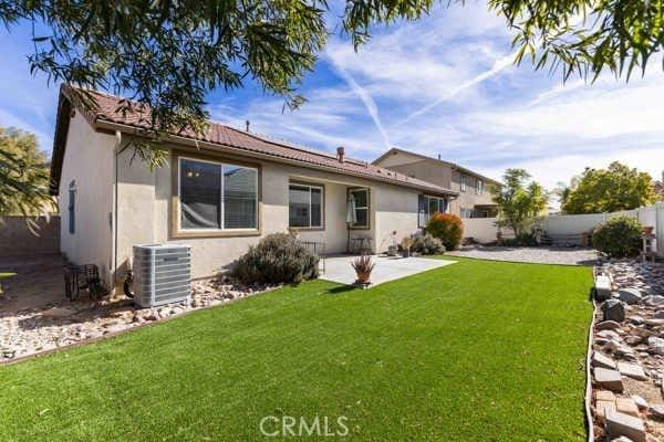 rear view of property with cooling unit, a patio area, and a lawn