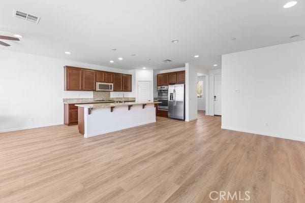 kitchen featuring appliances with stainless steel finishes, tasteful backsplash, an island with sink, a kitchen breakfast bar, and light hardwood / wood-style flooring