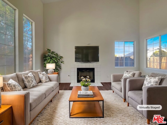 living room featuring hardwood / wood-style floors, a high ceiling, and a tiled fireplace