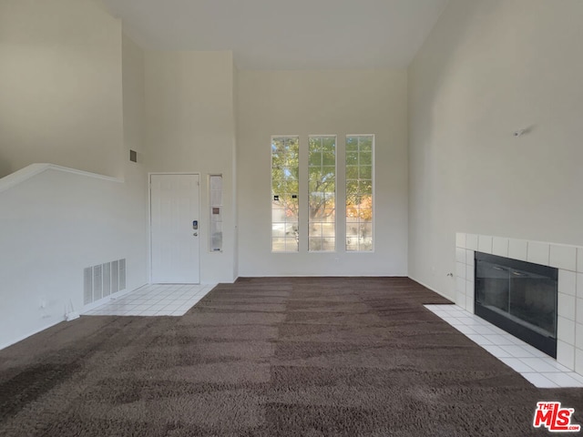 unfurnished living room with a tiled fireplace, light carpet, and a high ceiling