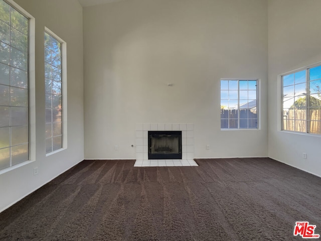 unfurnished living room featuring a fireplace, a towering ceiling, and dark carpet