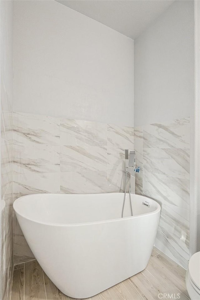 bathroom featuring hardwood / wood-style floors, a bathtub, tile walls, and toilet