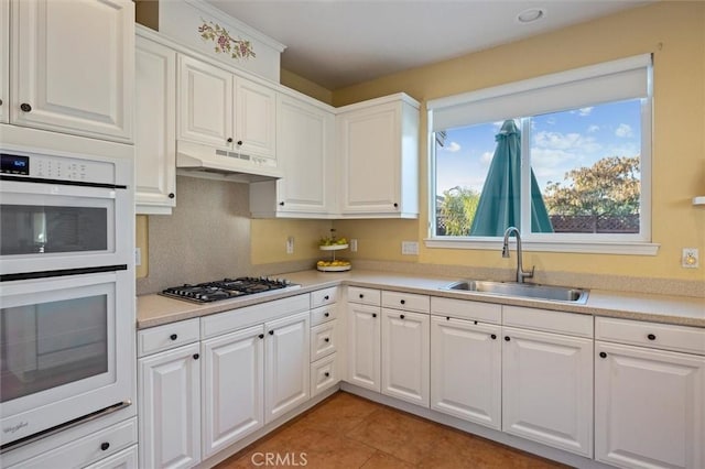 kitchen with white double oven, white cabinetry, light tile patterned flooring, stainless steel gas cooktop, and sink