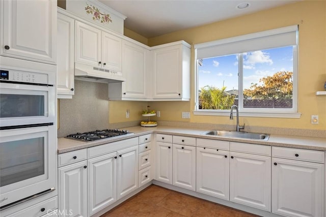 kitchen featuring stainless steel gas stovetop, white double oven, white cabinets, and sink