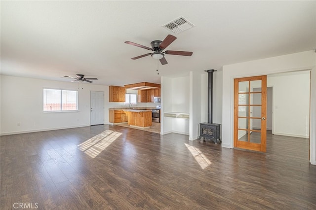 unfurnished living room with a wood stove, dark wood-type flooring, french doors, sink, and ceiling fan