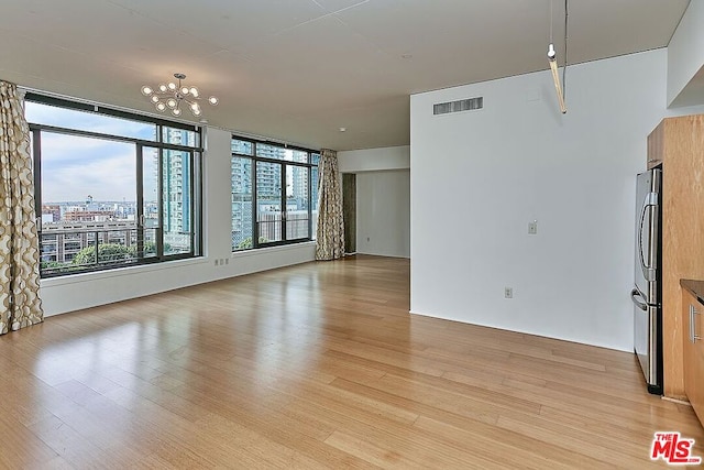 empty room with light wood-type flooring and an inviting chandelier