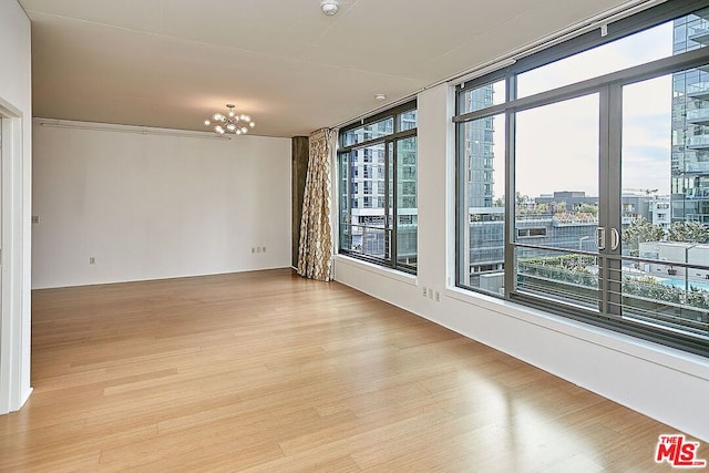 spare room with expansive windows, a chandelier, and light wood-type flooring