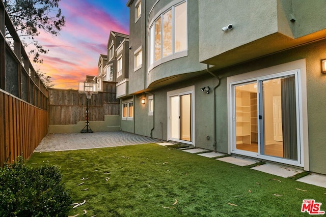 back house at dusk featuring a lawn and a patio