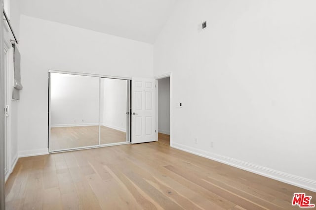 unfurnished bedroom featuring light hardwood / wood-style floors, high vaulted ceiling, and a closet