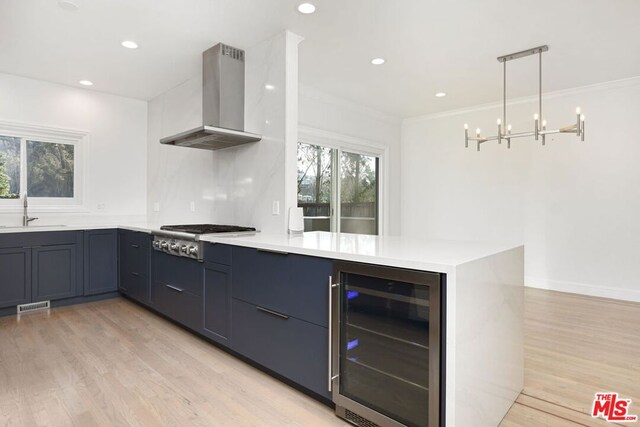 kitchen with hanging light fixtures, wall chimney exhaust hood, beverage cooler, and light wood-type flooring