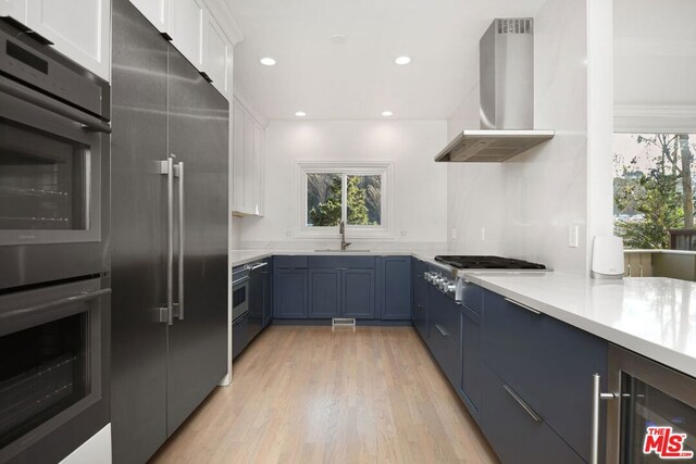 kitchen with sink, wall chimney exhaust hood, stainless steel appliances, wine cooler, and white cabinets